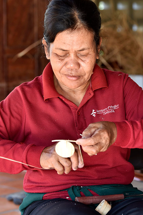 An artisan woman delicately weaves a craft box from palm branches.