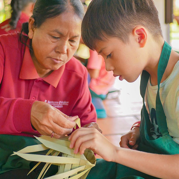 An old woman teaching a child how to weave palm leaves to create their own souvenir.