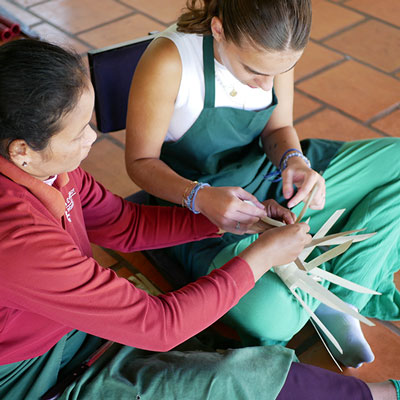 A visitor participates in a hands-on workshop at Senteurs d'Angkor, learning traditional weaving techniques with guidance from a local artisan.