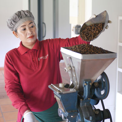 A woman at the Senteurs d'Angkor is pouring coffee beans into a grinder in a workshop.